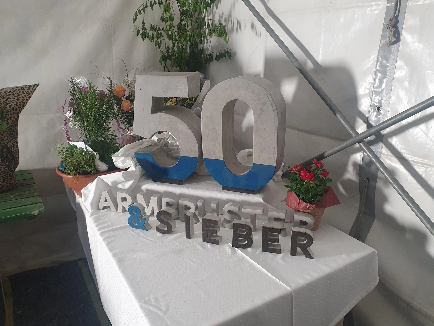 A&S Armbruster & Sieber GmbH - Experten im Bereich Bautenschutz und Bodenbeschichtungen - Dekorative Tischdekoration mit großer blau-weißer Zahl 50, Buchstabenblöcken mit der Aufschrift Armbruster & Steber und Topfpflanzen mit Blumen